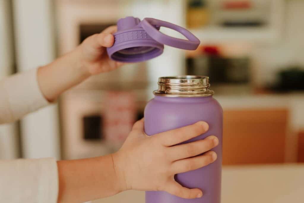 Little hands opening a purple water bottle.
