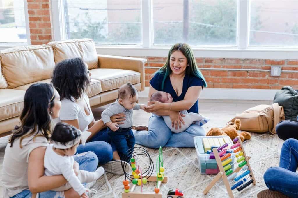 A group of women and babies sitting on the floor with baby toys.