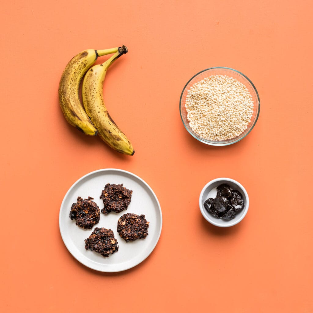 Three featured ingredients for healthy toddler breakfast cookies: bananas, puffed quinoa, and prunes, alongside a plate of the finished cookies.