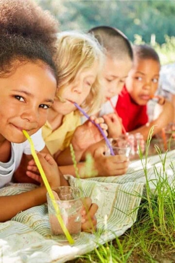 A row of kids sitting on their stomachs, propped up on elbows, drinking from straws.