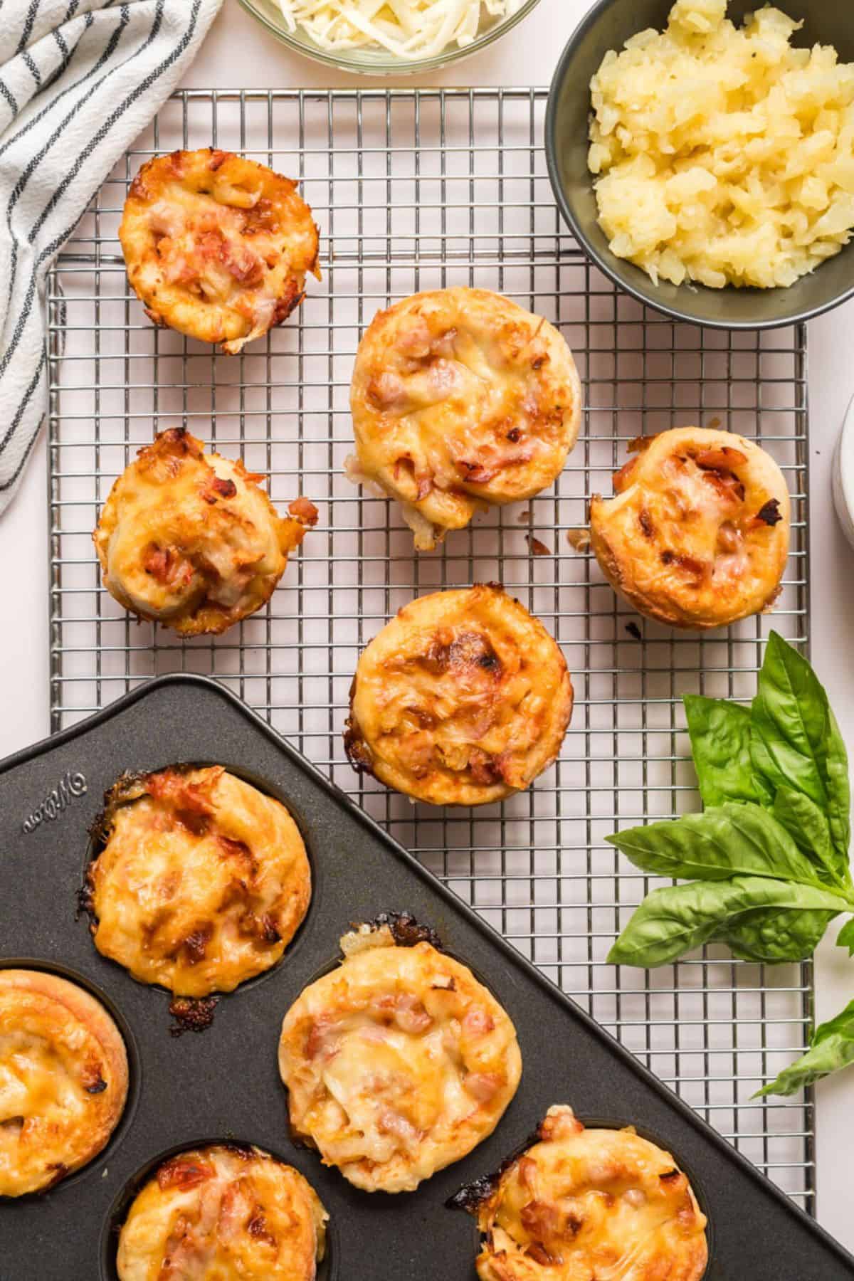 Pizza rolls that have been baked and spread out on a cooling rack with garnishes such as pineapple, ham and cheese. 