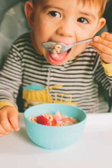 Toddler bringing a spoon to his mouth in high chair.