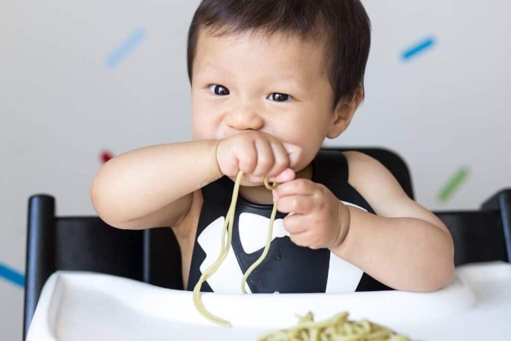 A baby in a high chair enjoying spaghetti.