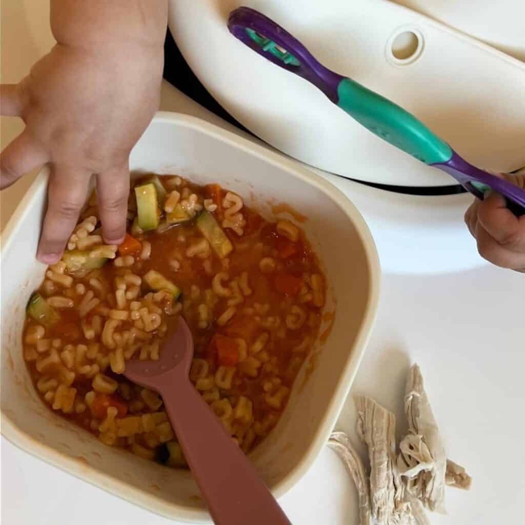 A baby reaching into a bowl of sopita de verduras.