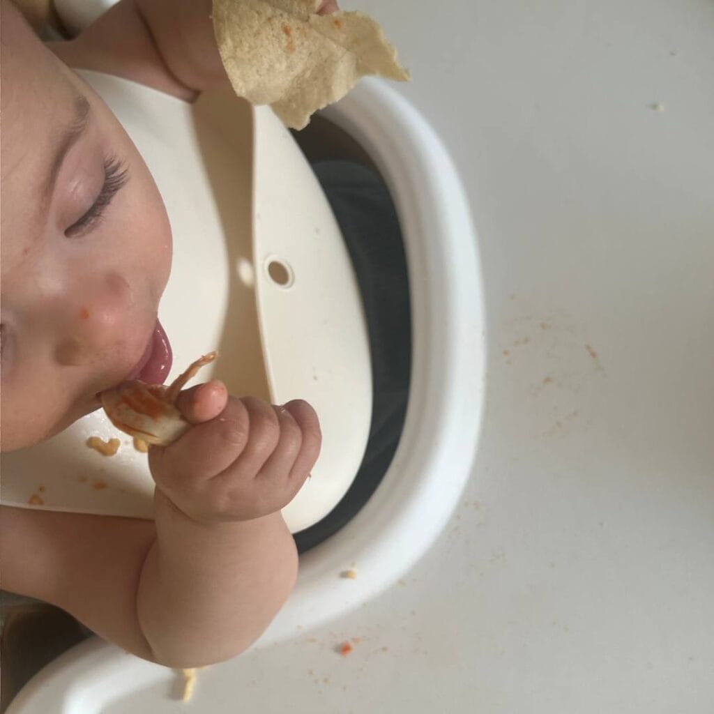A baby in a high chair enjoying chicken tinga, adapted to be baby friendly.