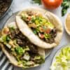 Two pitas stuffed with tender pull apart sumac beef with caramelized onions along with chopped lettuce & tomatoes, drizzled with almond tahini sauce.