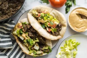 Two pitas stuffed with tender pull apart sumac beef with caramelized onions along with chopped lettuce & tomatoes, drizzled with almond tahini sauce.