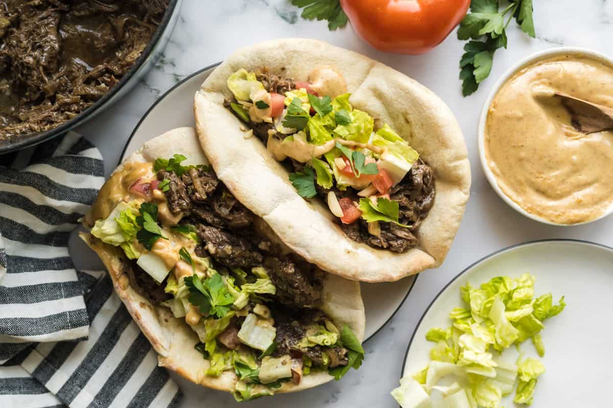 Two pitas stuffed with tender pull apart sumac beef with caramelized onions along with chopped lettuce & tomatoes, drizzled with almond tahini sauce.