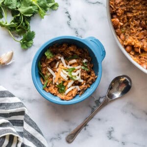 A toddler bowl of sofrito beef, beans, and rice beside a pot of the same dish.