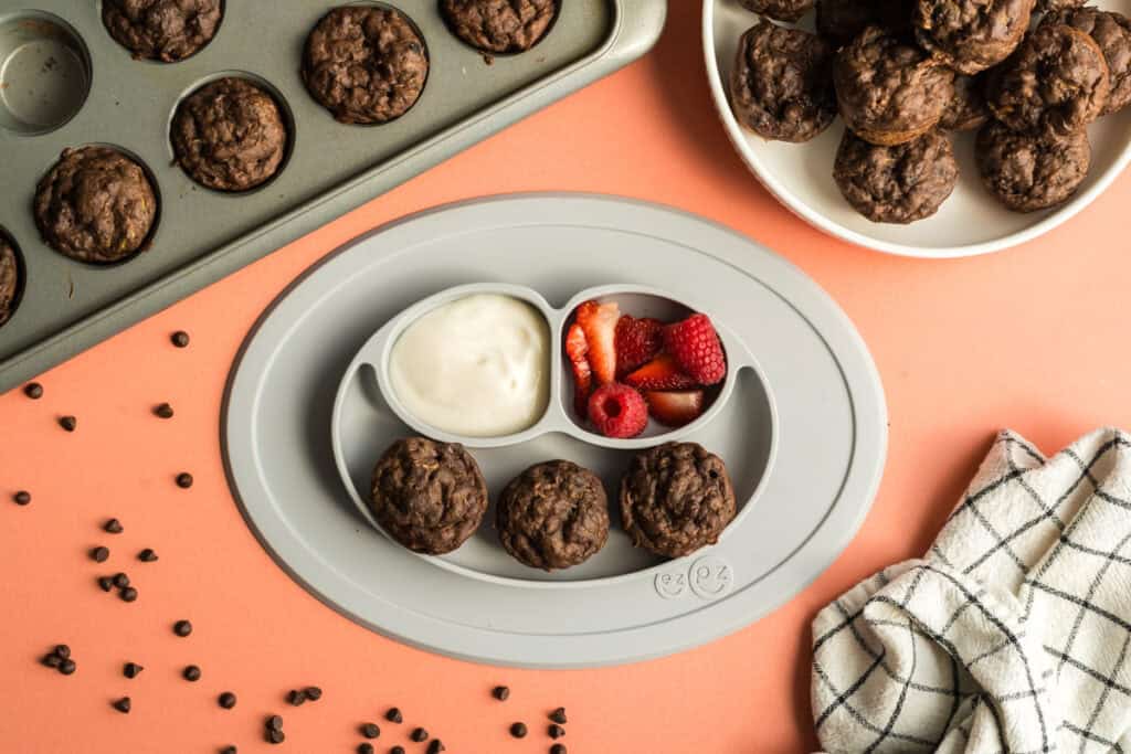 A divided plate with a balanced toddler snack - healthy double chocolate mini muffins (with black beans and zucchini) + cut up strawberries, and yogurt.