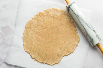 Whole wheat and lower sugar fruit pizza crust rolled out on a piece of parchment paper.