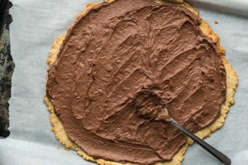 Cooked and cooled fruit pizza crust dough that has sauce spread on top. The sauce is chocolate cream cheese. 