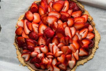A lower sugar toddler friendly fruit pizza topped with chocolate cream cheese sweetened naturally by dates, and topped with fresh strawberry slices. 
