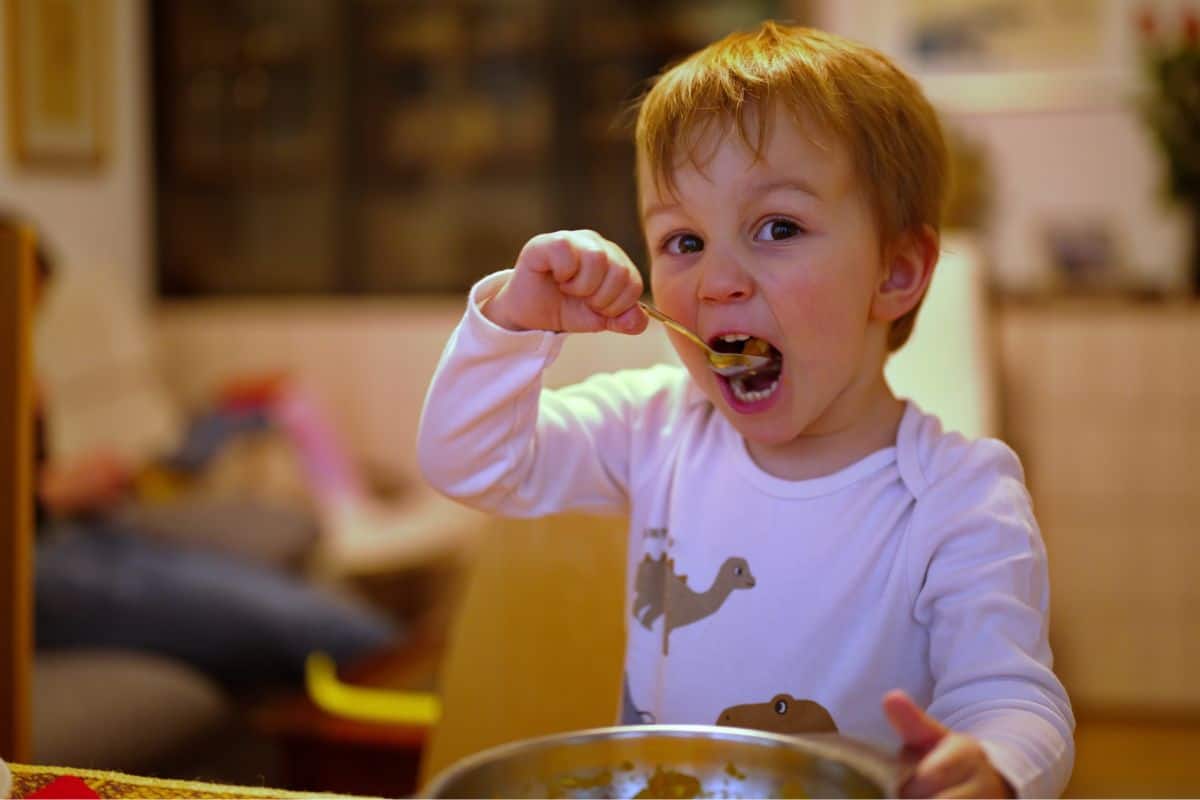 A toddler bringing a spoon to his mouth.