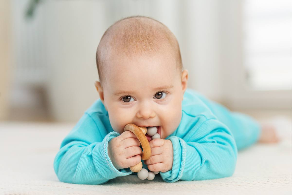 Baby lying on tummy gumming a wooden teether toy.