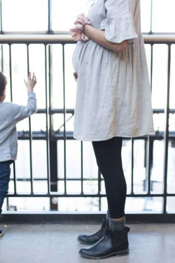 PRegnant woman holding her belly with a toddler by her feet.