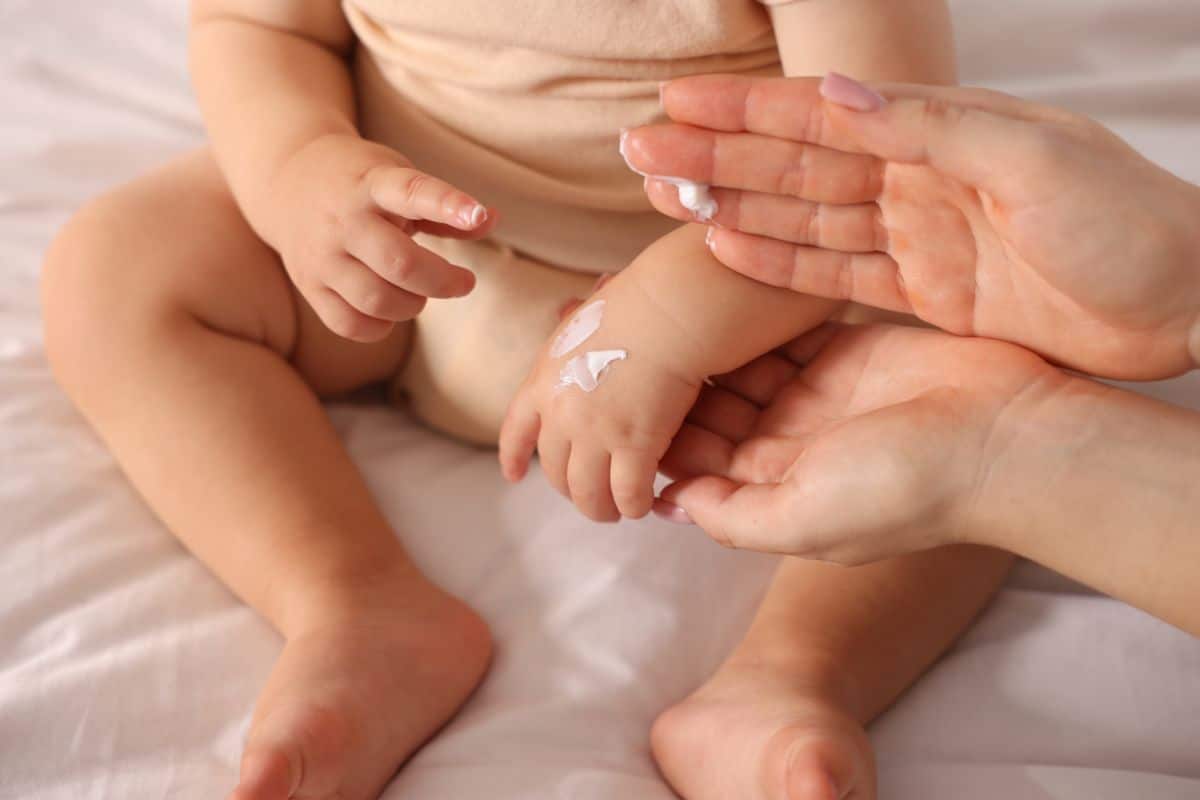 a mother's hand applying lotion to a baby's hand.