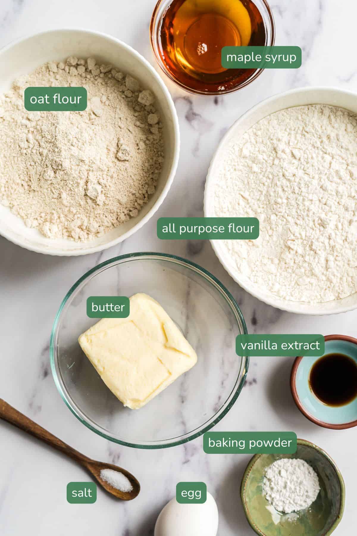 ingredients for homemade animal crackers arranged on a table including maple syrup, oat flour, flour, butter, vanilla and salt. 