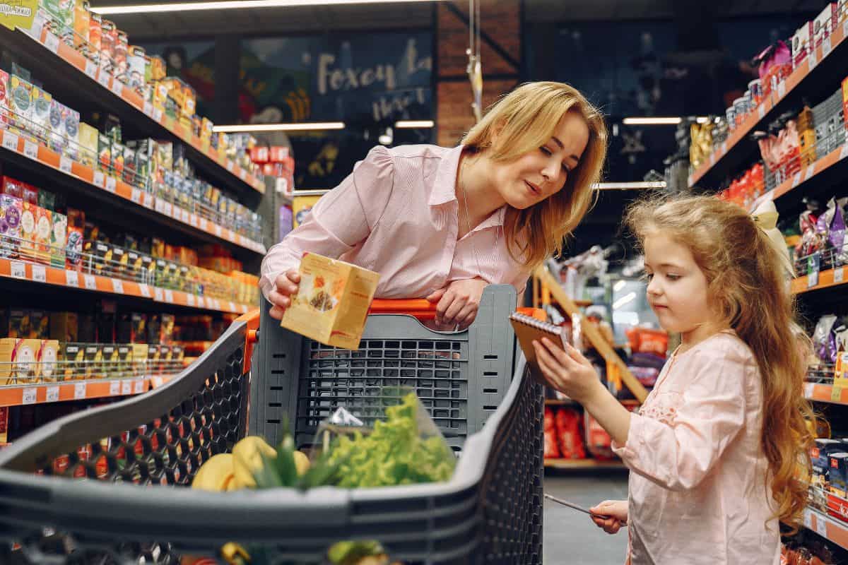 Mom and girl looking at grocery list pushing a grocery cart in store.
