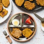 A baby plate with sweet potato fritters spread with a thin layer of almond butter, hardboiled egg, and a strawberry.