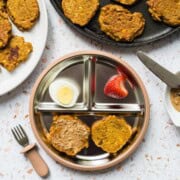 A baby plate with sweet potato fritters spread with a thin layer of almond butter, hardboiled egg, and a strawberry.