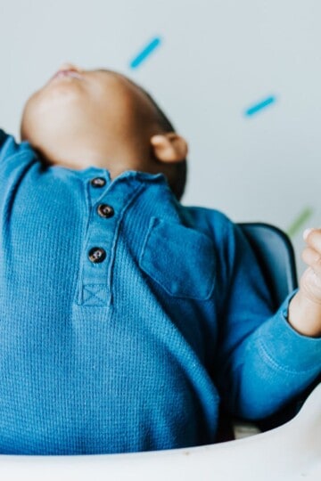 Baby in a high chair arching his back and appears to be throwing or protesting eating food.