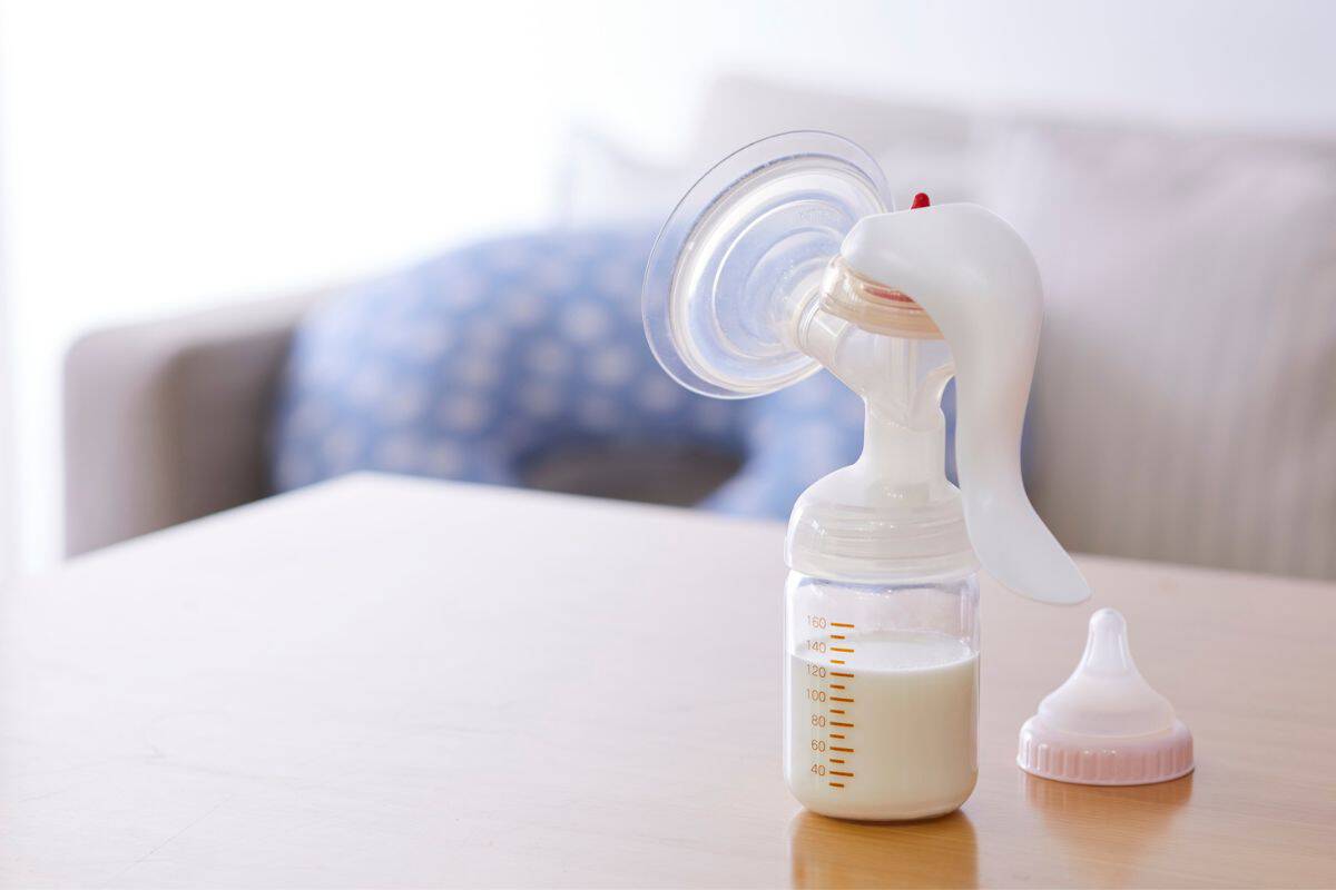 Expressed breastmilk in a manual breast pump on a table with a baby nipple beside it.