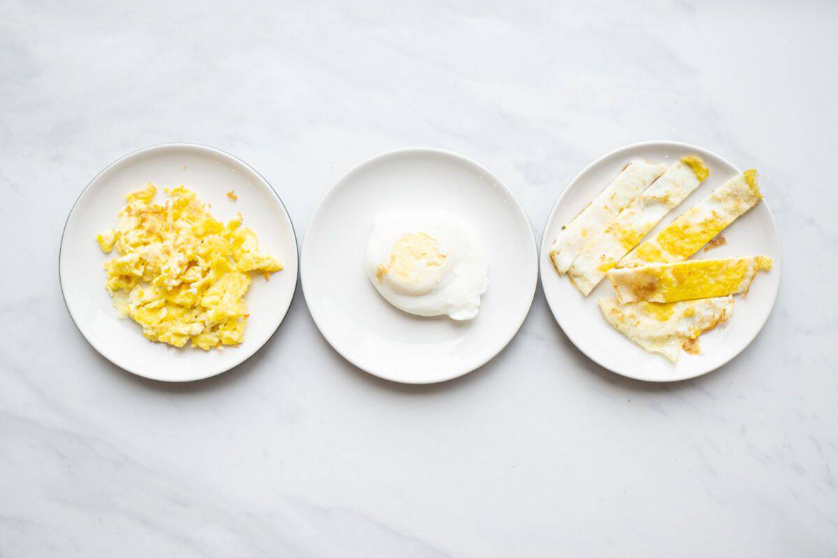 Flatlay of of three small dishes with a different variation of egg for a baby. From left to right there is an example of scrambled eggs, poached egg and fried egg sliced in strips.