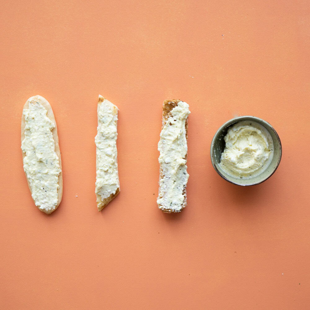 Flat lay of different puree egg options. From left to right, there is egg puree on a baby rusk, flat bread, toast and a small portion of egg puree in a bowl.