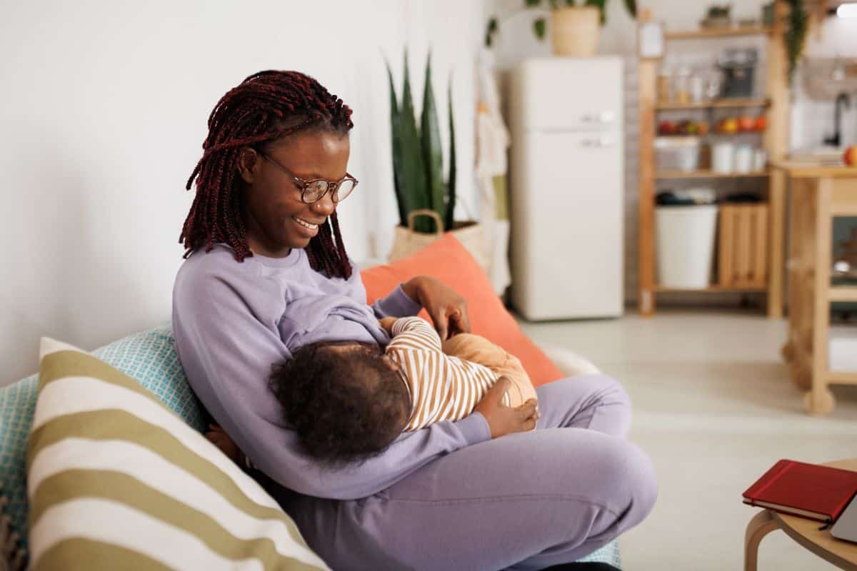 woman sitting on a couch cuddling her baby and breastfeeding.