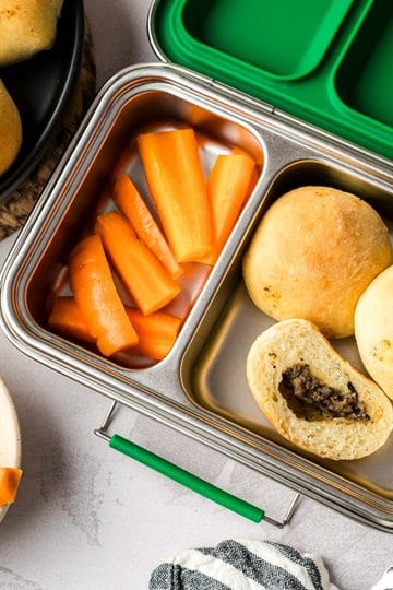 Three Mennonite meat buns in a lunchbox with cut carrots.