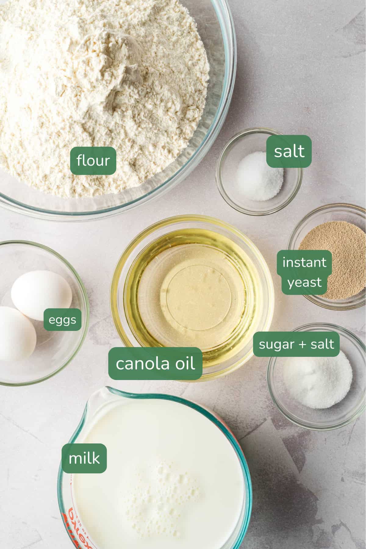 flat lay of dough recipe ingredients for meat buns: flour, salt, sugar, milk, oil, nutritional yeast and egg.
