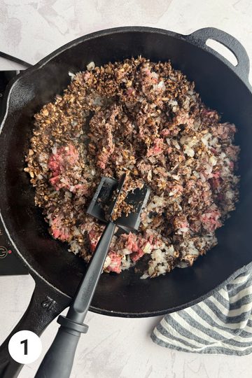 Skillet with mushrooms, onions, ground beef, garlic powder, and salt being sauteed.
