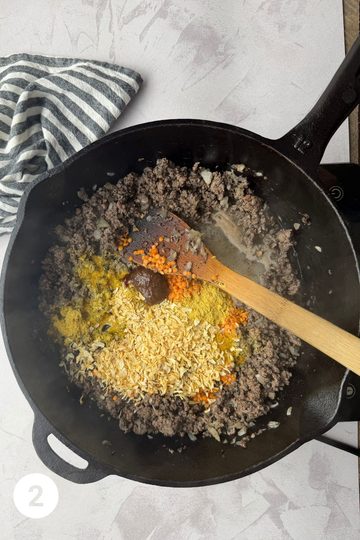 Skillet with the meat filling mixture except in this step there is now beef boullion, nutritional yeast, spices and split red lentils in the pan.