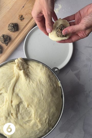 Hands that are preparing a mennonite meatbun - there is a flattened piece of dough with meat filling inside that is about to be pinched into a ball.
