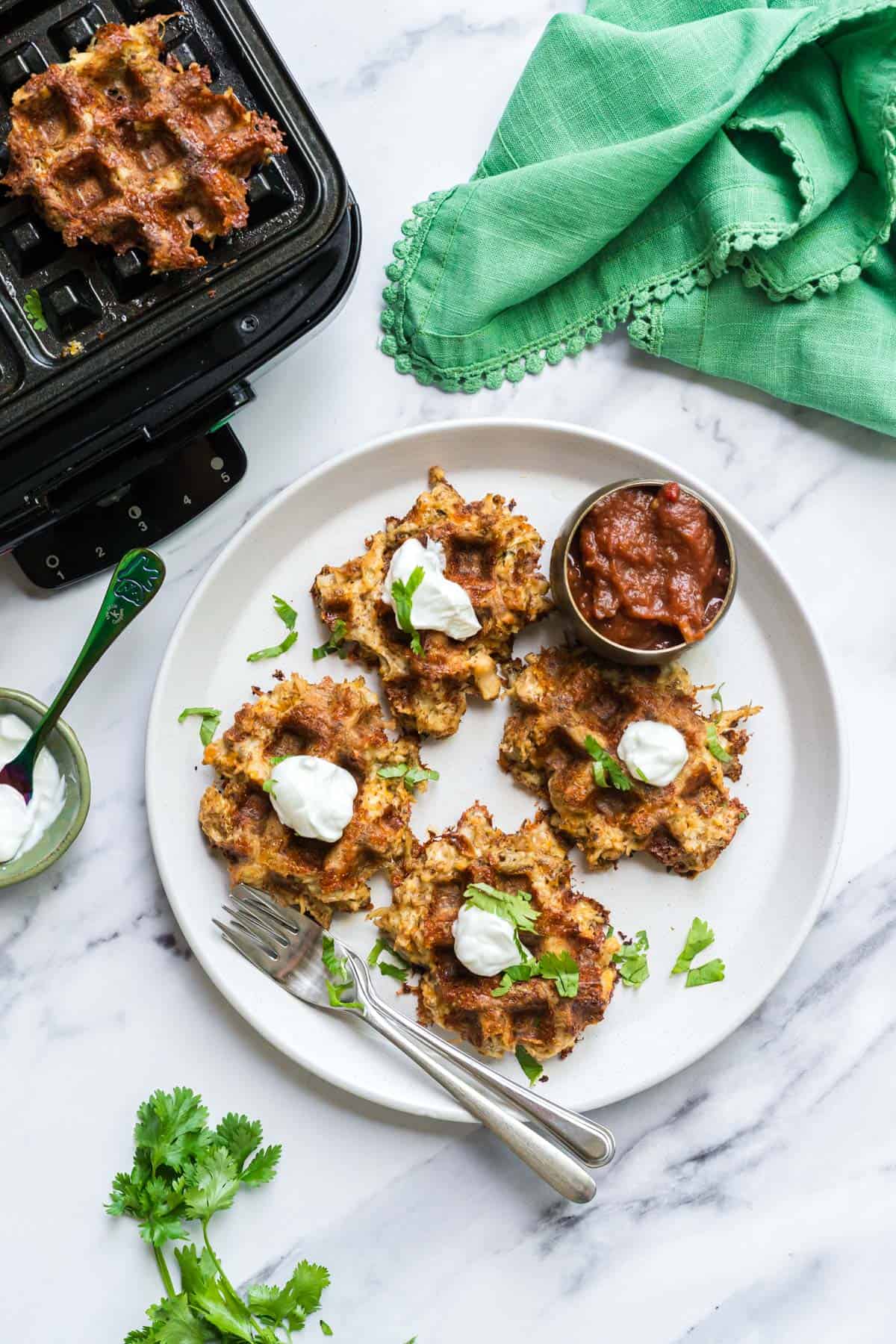 Chicken taco waffles on a plate with dollops of sour cream on top and a small bowl of salsa for dipping.