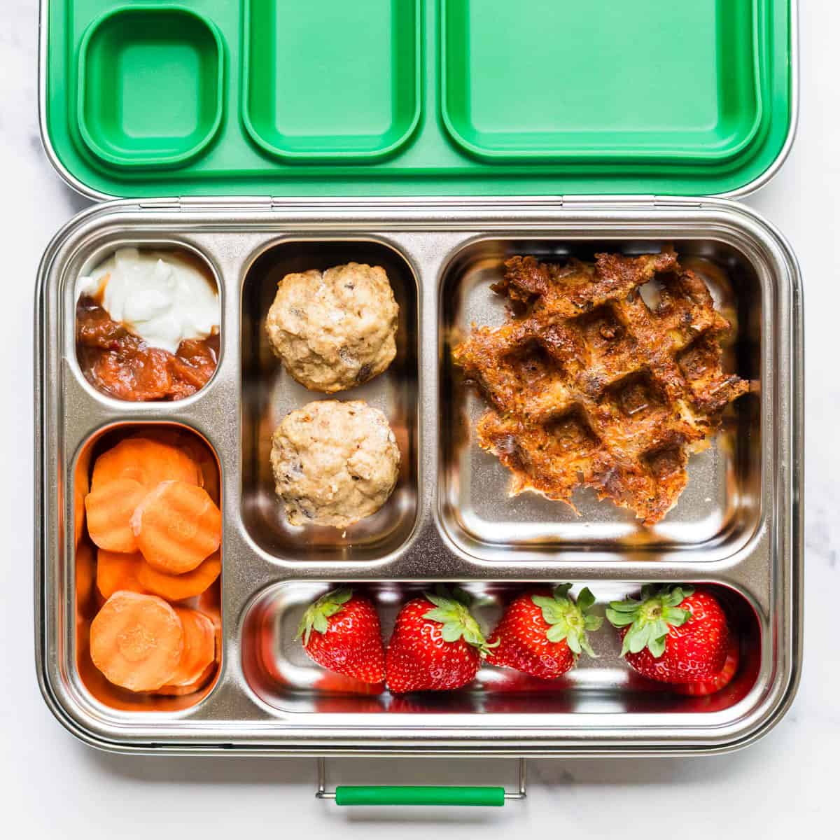 Lunch box with chicken taco waffles, salsa/sour cream for dipping, carrots, strawberries, and banana muffins