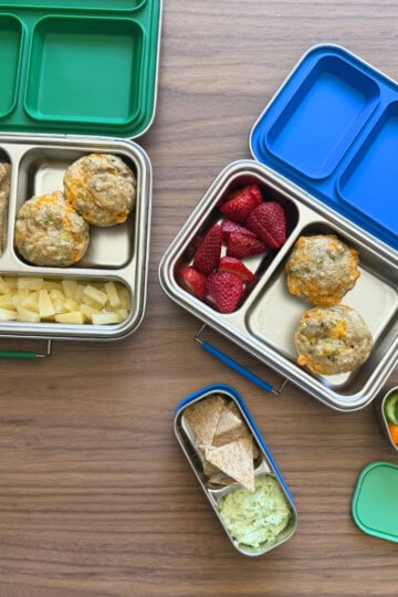 Two lunch kits for children filled with cucumbers, crackers, canned pineapple, broccoli cheddar egg muffins and another lunch kit with raspberries and the broccoli cheddar egg muffins.