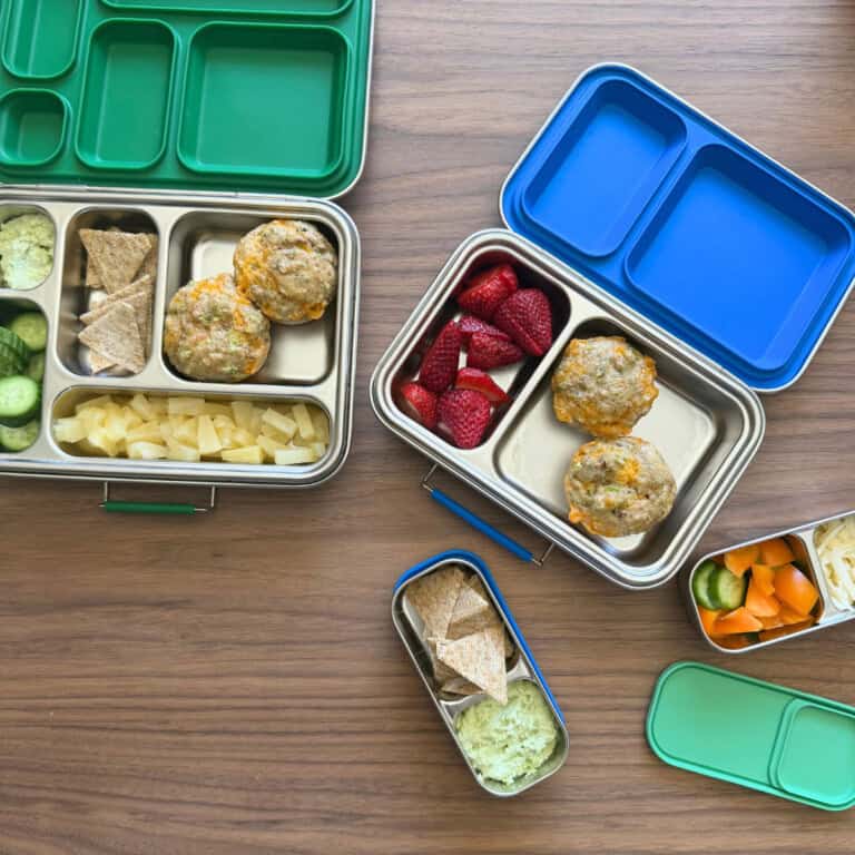 Two lunch kits for children filled with cucumbers, crackers, canned pineapple, broccoli cheddar egg muffins and another lunch kit with raspberries and the broccoli cheddar egg muffins.