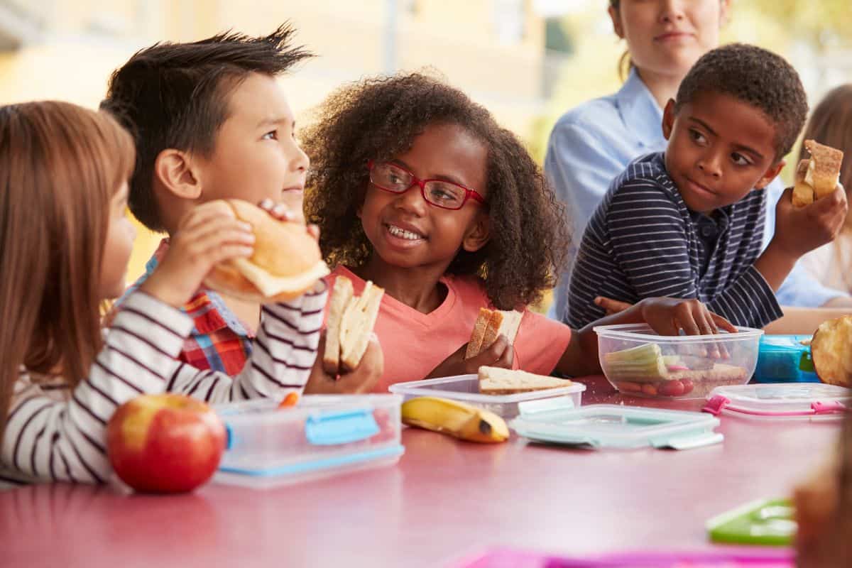 Elementary aged children eating packed lunches at a table.